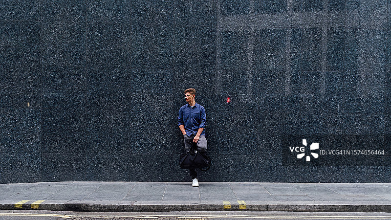 背景中靠在暗墙上的年轻男子图片素材