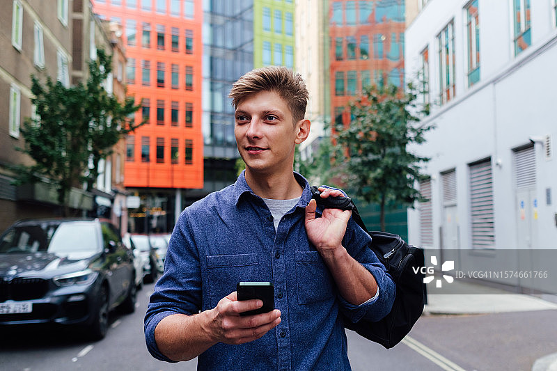 拿着手机和背包走在街上的年轻人图片素材