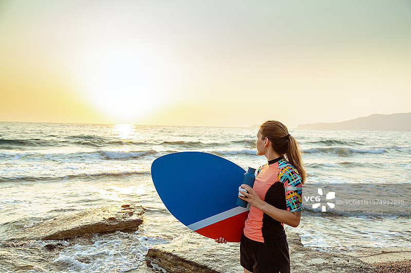 在海滩上休息并眺望地平线的年轻白人女性滑板爱好者图片素材