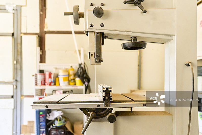 空旷木工车间工作台上无人使用的锯床，正面视角图片素材
