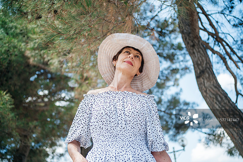 戴着草帽，在夏日花园里享受阳光的年长女性图片素材