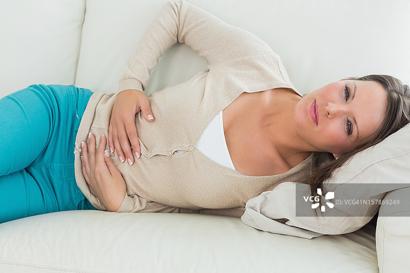 女人因胃部不适躺在沙发上图片素材