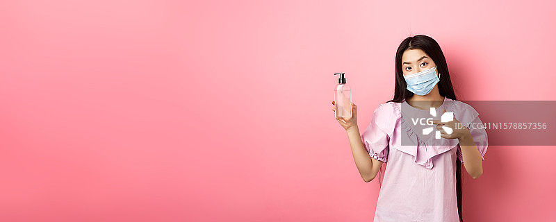 戴口罩的时尚女孩展示消毒液，粉色背景图片素材