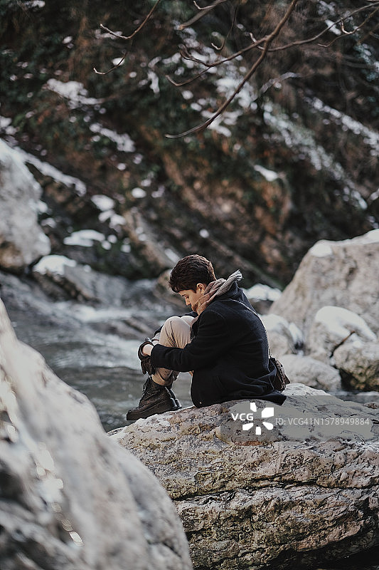 男子坐在俄罗斯克拉斯诺达尔边疆区索契森林的岩石上拍照的侧视图图片素材
