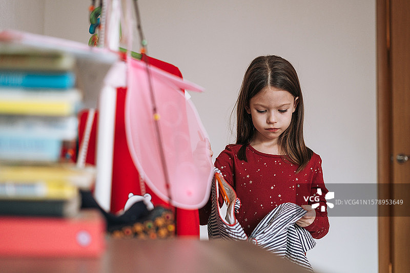 穿着红色连衣裙的小女孩在自己房间的衣柜里挑选漂亮的连衣裙图片素材