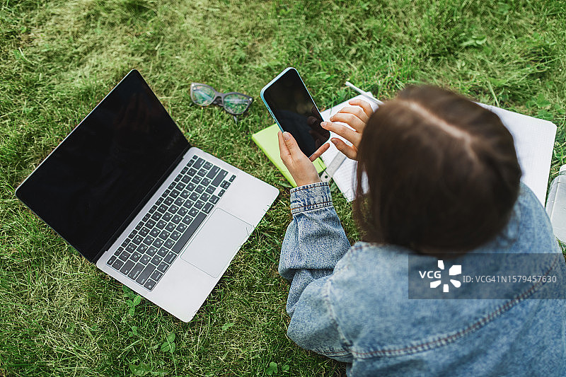 女大学生在校园草坪上用笔记本电脑和笔记本做作业图片素材