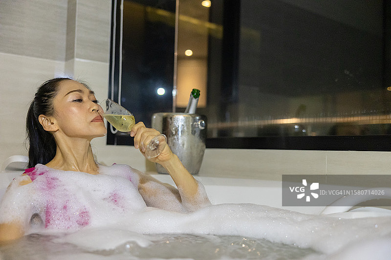 宁静的水疗休憩：亚洲女子享受泡澡时光，品味美酒图片素材