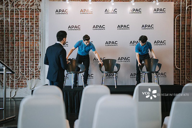 亚洲宴会厅经理在商务会议研讨会开始前协调工作人员在舞台上安排贵宾席位图片素材