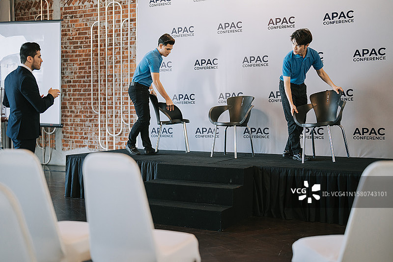 亚洲宴会厅经理在商务会议研讨会开始前协调工作人员在舞台上安排贵宾席位图片素材