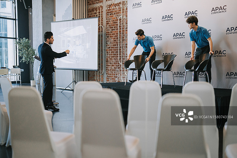 亚洲宴会厅经理在商务会议研讨会开始前协调工作人员在舞台上安排贵宾席位图片素材