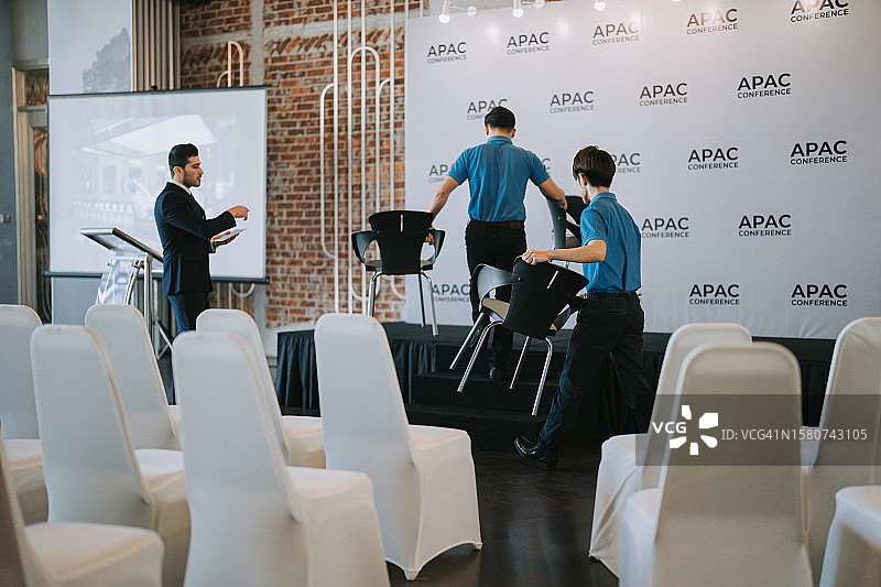 亚洲宴会厅经理在商务会议研讨会开始前协调工作人员在舞台上安排贵宾席位图片素材