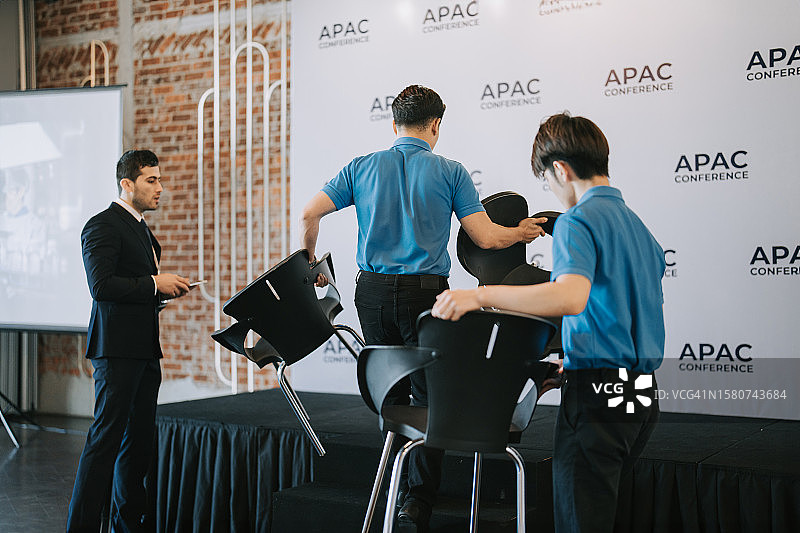 亚洲宴会厅经理在商务会议研讨会开始前协调工作人员在舞台上安排贵宾席位图片素材