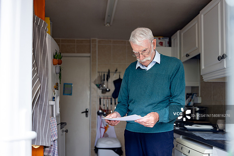 年长的男人在他家的厨房里读信图片素材