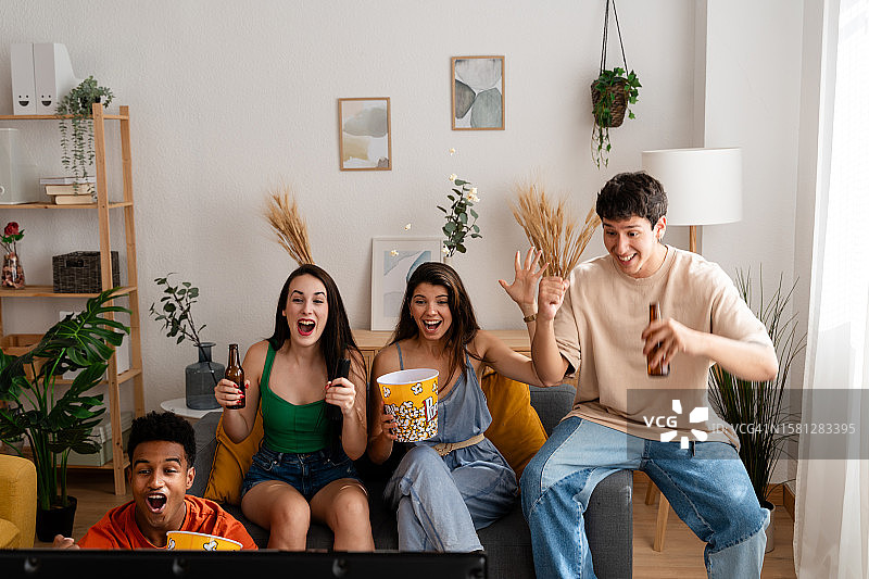 朋友们在家里的客厅里一边吃着爆米花一边看电影庆祝图片素材