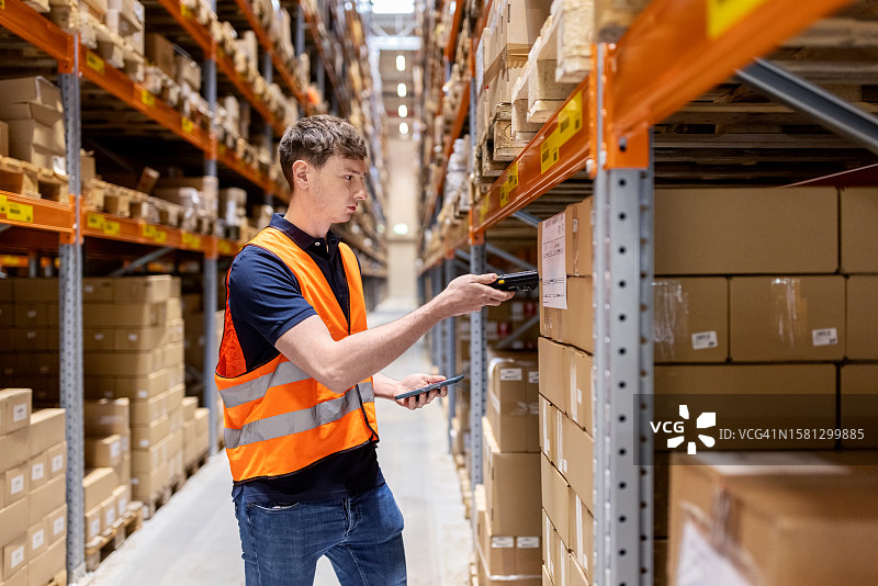 年轻的仓库工人用便携式扫描仪扫描货架上的产品包装盒图片素材