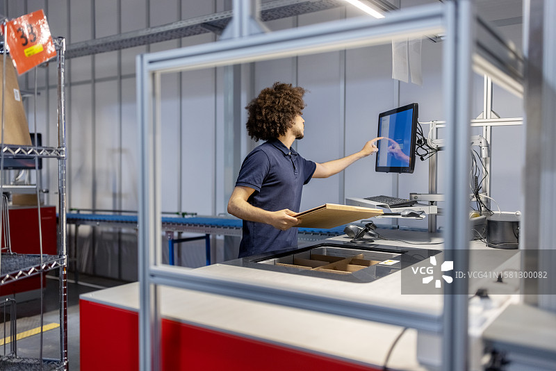 在自动化仓库中，年轻男人拿着盒子在电脑上更新包裹详情图片素材