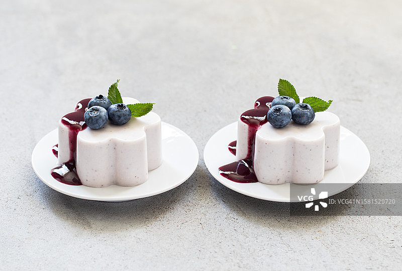 盘子上放着两份蓝莓意式奶冻和酱汁。浅灰色背景图片素材