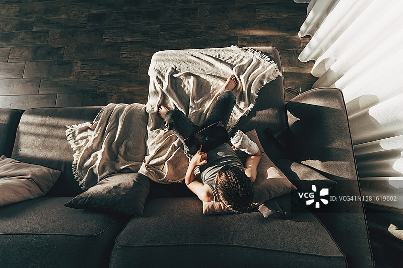 受伤的男孩躺在沙发上，手臂骨折打着石膏图片素材