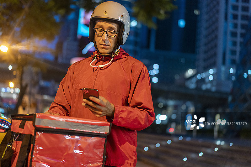 黄昏时看着智能手机的送货员图片素材