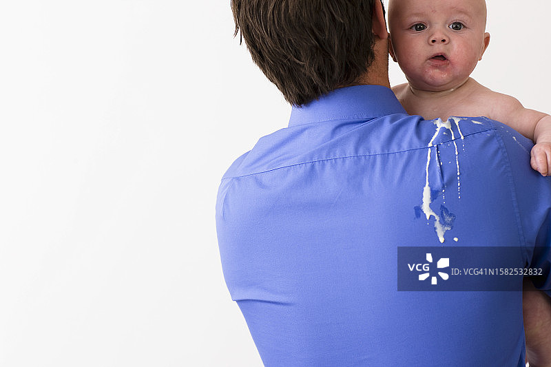 男子抱着背部和肩膀沾有呕吐物的婴儿的背影图片素材