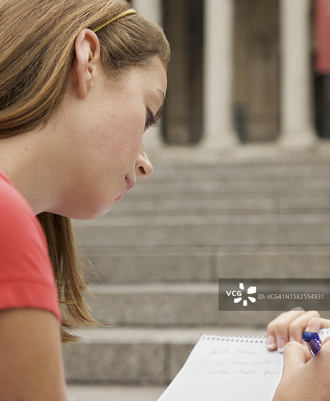 在城市建筑对面做笔记的少女图片素材