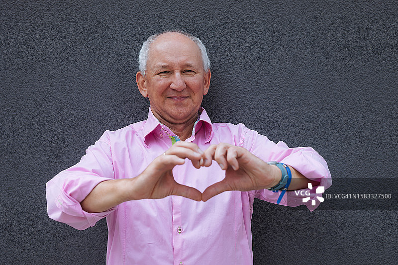 穿着亮粉色衬衫，用双手做出心形的年长男人图片素材