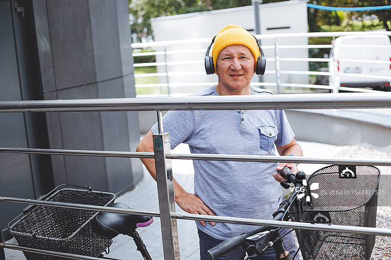 戴着黄色无檐小便帽和无线耳机的老年绅士准备骑自行车图片素材