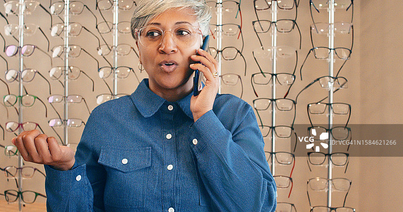 电话沟通，老年妇女在商店购物，挑选眼镜。使用智能手机与配镜店的联系人进行眼科咨询图片素材