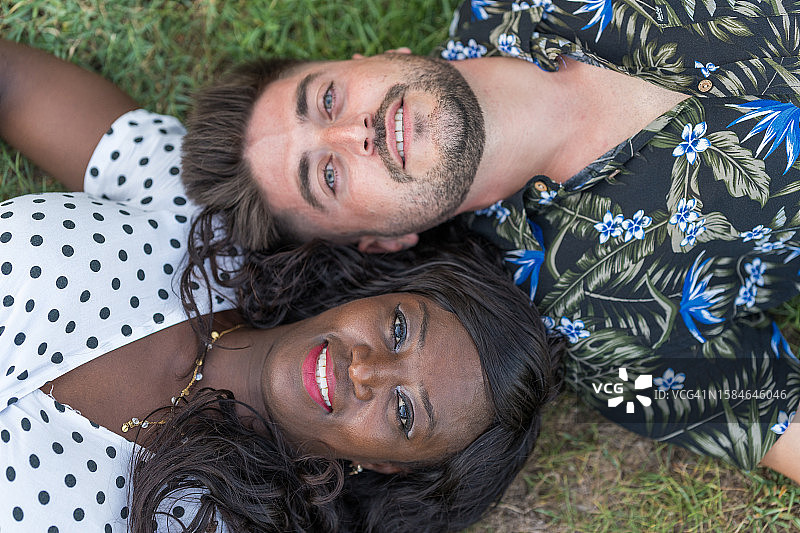 跨种族情侣躺在草地上看着镜头图片素材