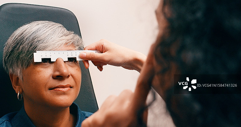 眼科护理：老年妇女用尺子测量视力配眼镜图片素材