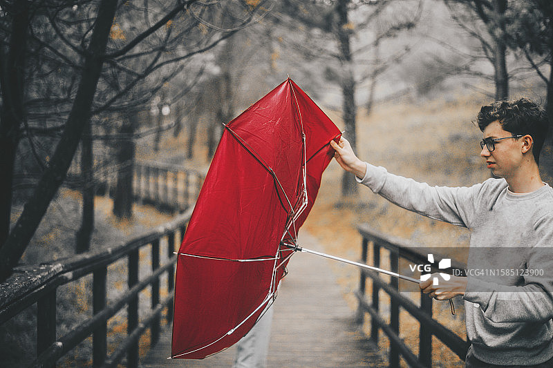 在刮风的天气里，一个年轻男人没能控制住他的伞图片素材