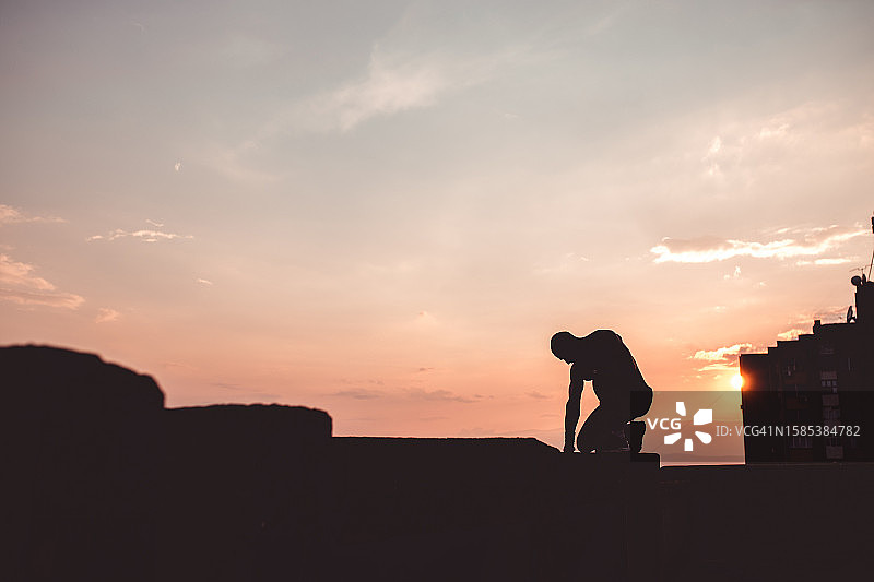 日落时分站在建筑物边缘的健壮男人图片素材