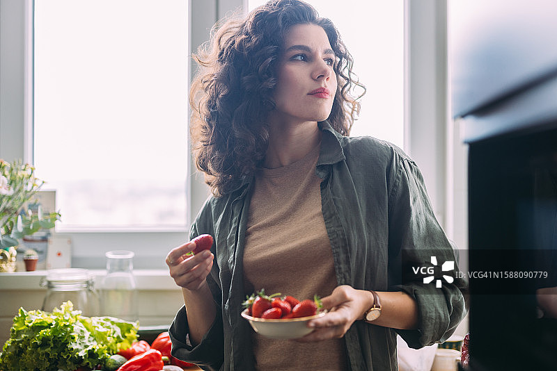 快乐的女人吃草莓时看向别处图片素材