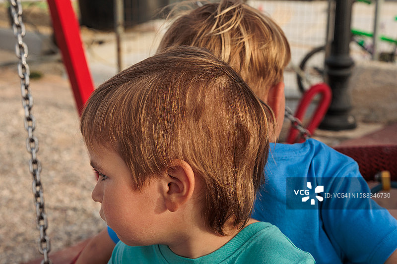 公园里背靠背坐在游乐设施上的小兄弟，因秋千争吵图片素材