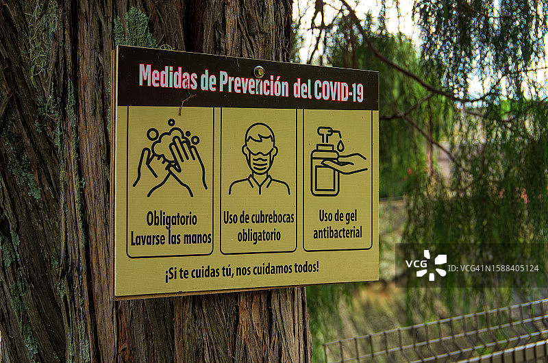 公园树干上的西班牙语Covid-19预防措施标志图片素材