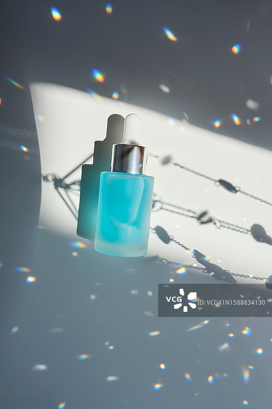 白色背景下带有虹彩高光的蓝色面部精华液瓶图片素材