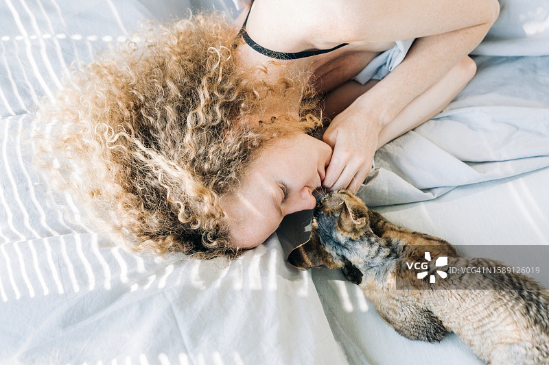 女子在家中床上睡觉：猫咪叫醒在床上睡觉的主人图片素材