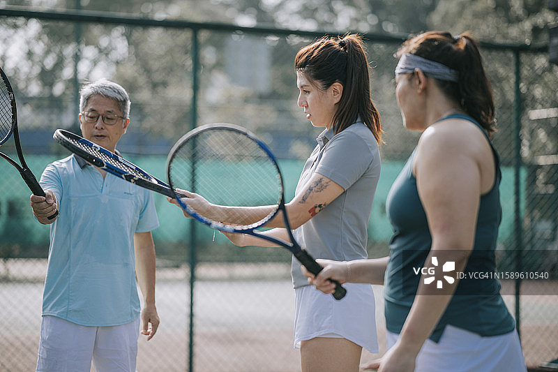 亚洲网球教练指导成年学员在网球场上握球拍图片素材