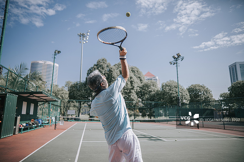 老年亚洲男人在网球场发球图片素材