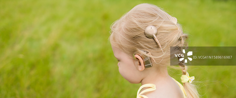 带着人工耳蜗走路的有趣宝宝。助听器和医学创新技术与多样性概念。横幅图片素材