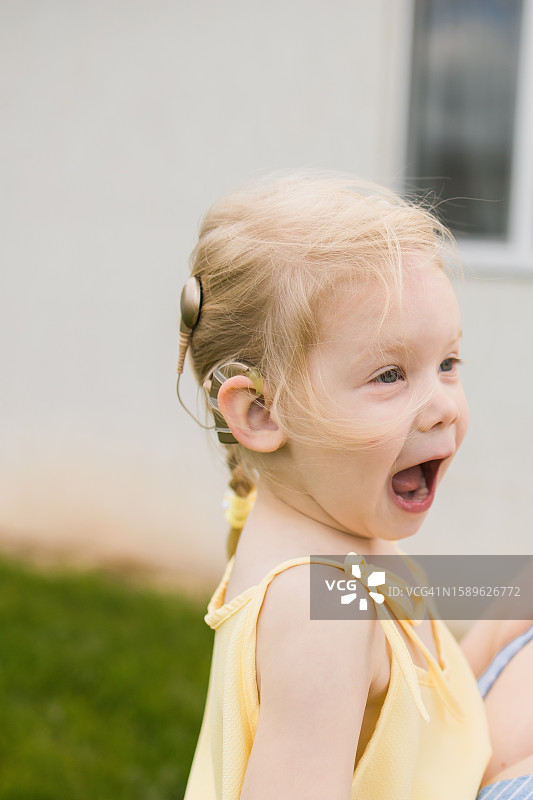 带着人工耳蜗，笑着听的小女孩。听力障碍儿童的适应图片素材