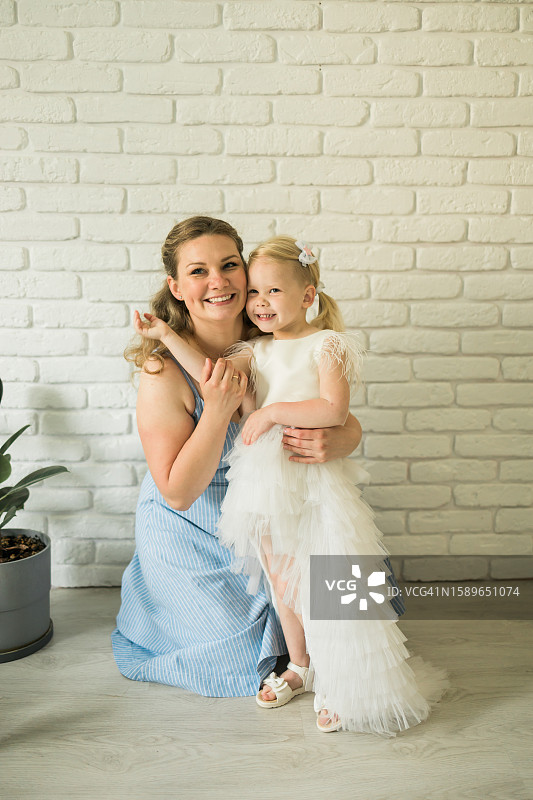 节日盛装的母女在砖墙背景的房间里微笑拥抱图片素材