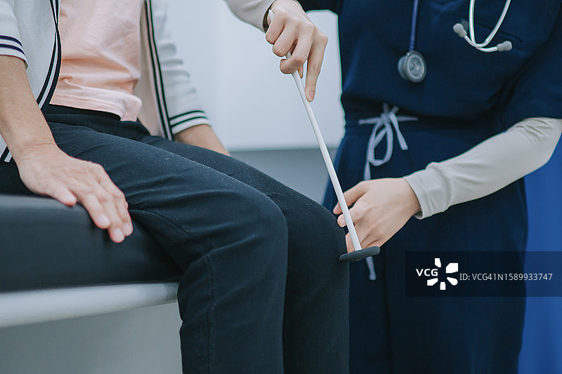 中国女医生用反射锤在诊所检查老年妇女的膝盖神经系统图片素材