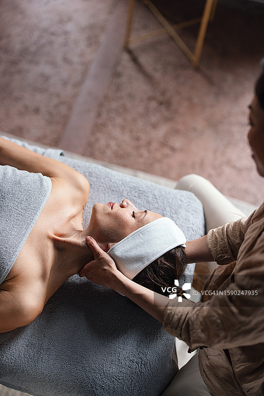 在水疗中心为仰卧美女进行颈部按摩的匿名按摩师图片素材