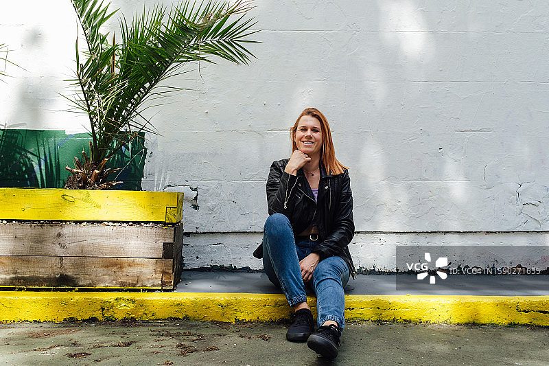 一位放松的红发女人坐在人行道上看相机图片素材