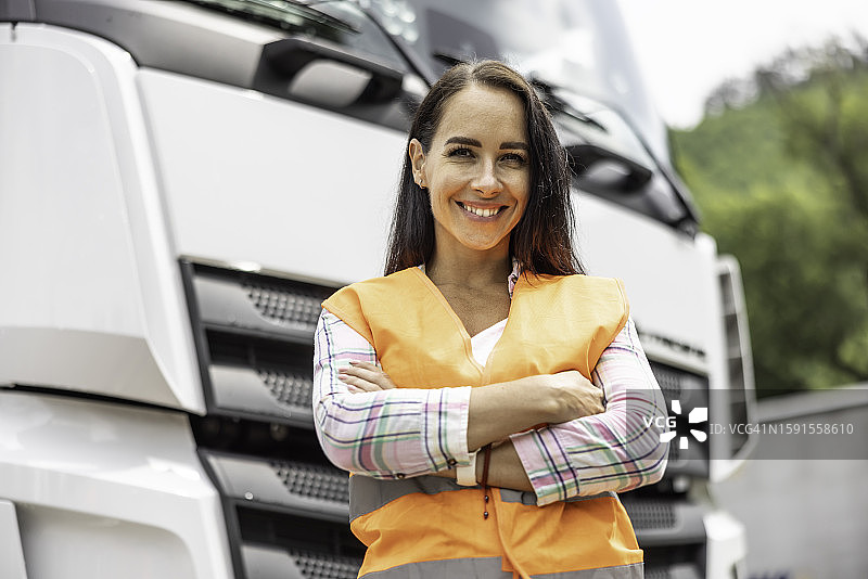 微笑的女人穿着橙色安全背心站在半挂卡车前图片素材