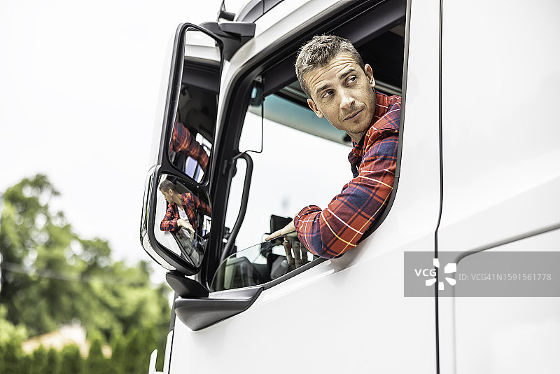 半挂卡车司机倒车到装货点时，从驾驶室的敞开式车窗向后看。图片素材