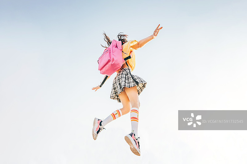 无忧无虑的女学生张开双臂，背着粉色背包在蓝天下跳跃图片素材
