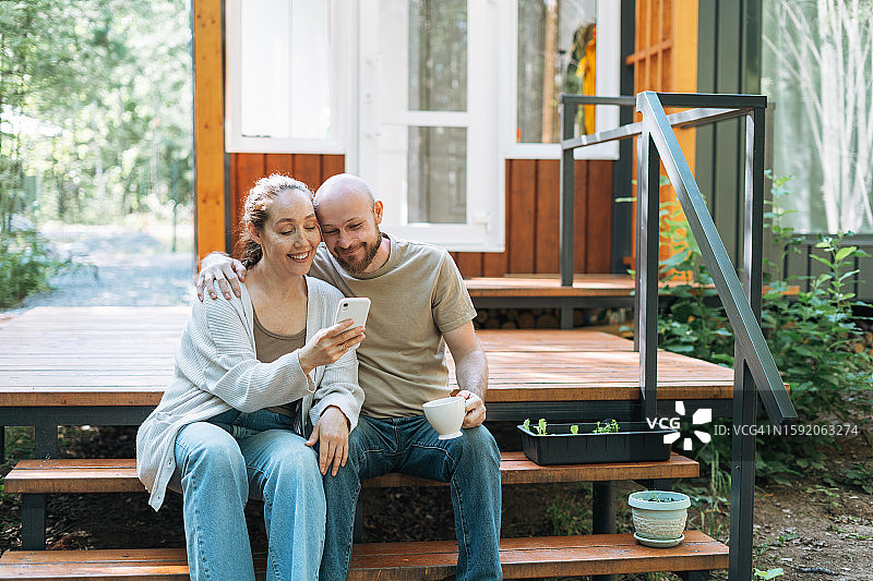 一家人在乡间别墅的后院喝早咖啡和使用手机图片素材