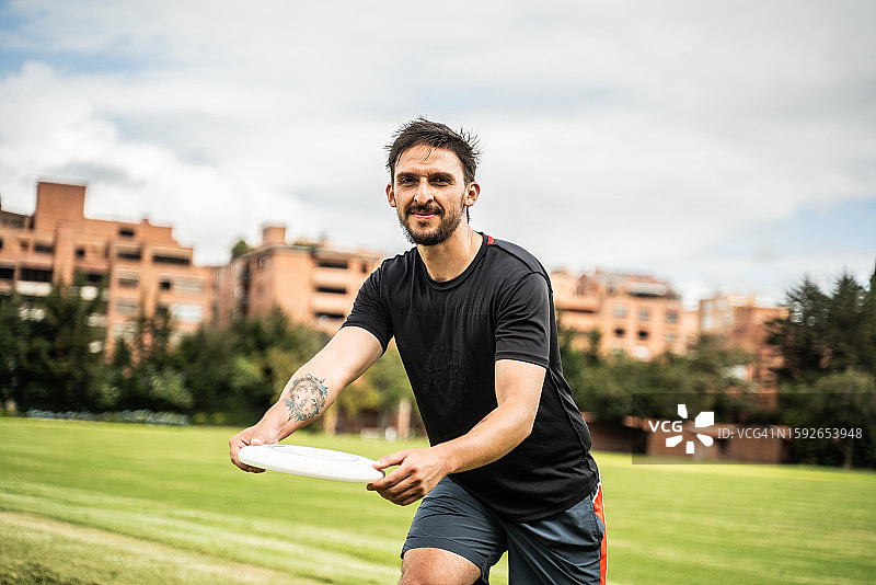 年轻男子在公园里扔飞盘的肖像。图片素材